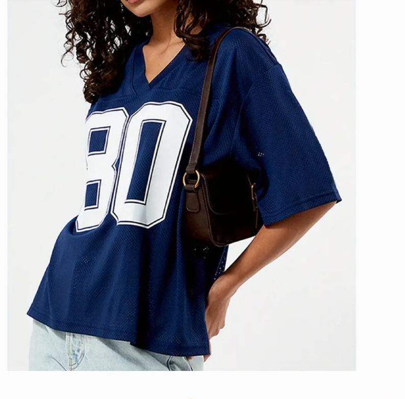 Model wearing a graphic jersey t-shirt in navy blue with number 80, holding a small handbag.