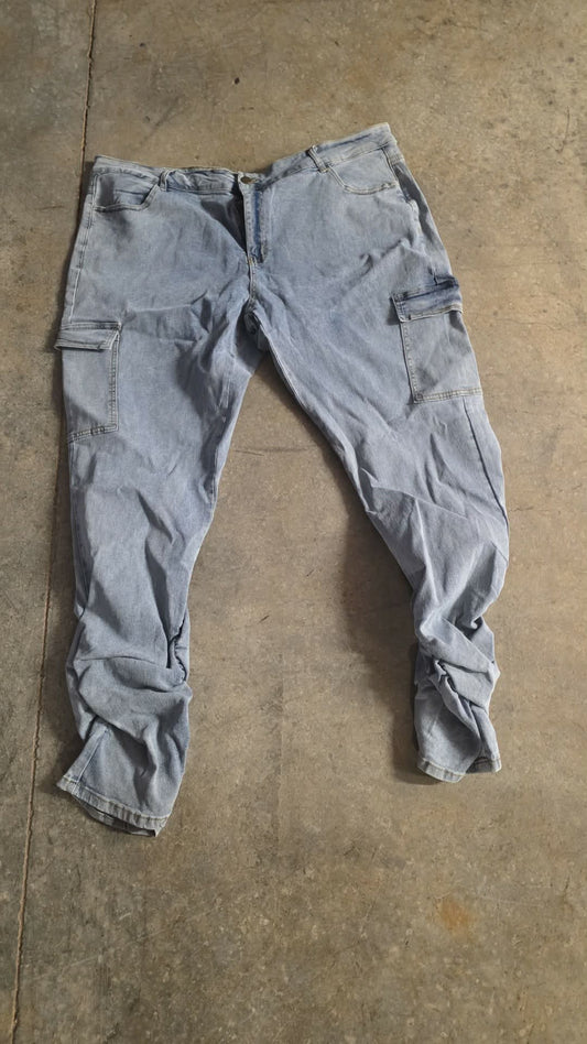 Plus cargo stacked jeans displayed on a concrete floor, featuring multiple pockets and a relaxed fit.